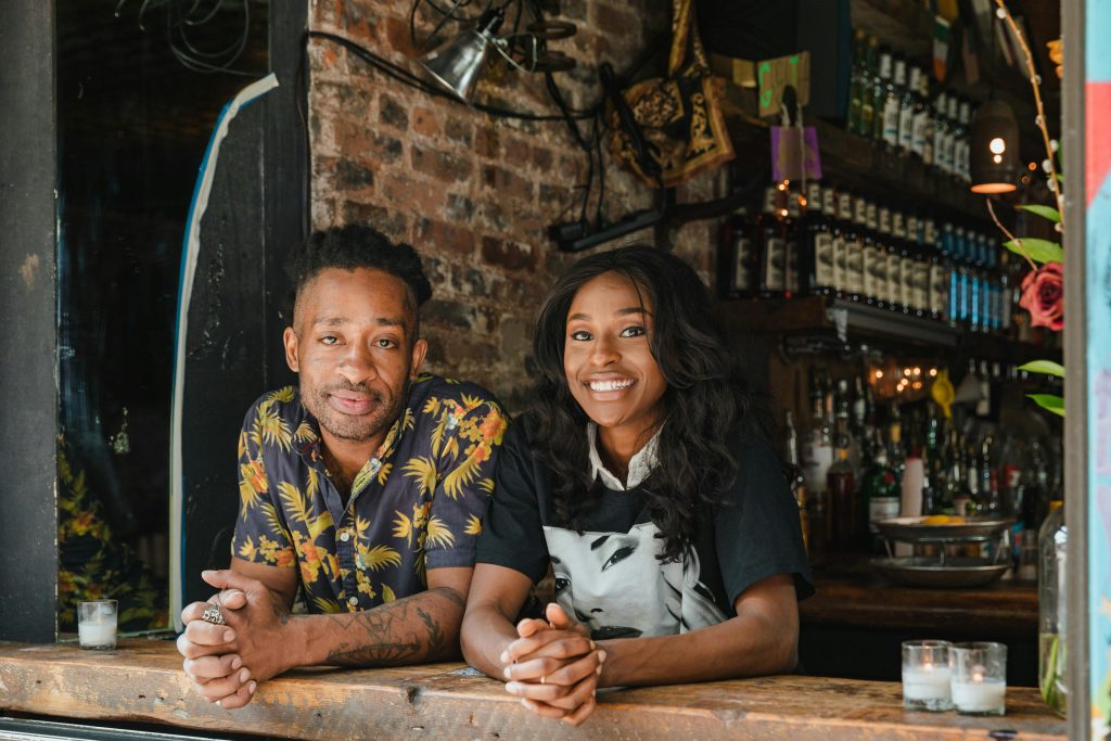 A cheerful couple dressed casually at the counter of a cozy cafe, surrounded by warm decorations.